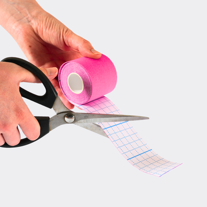 Person holding pink tape and scissors with a white background