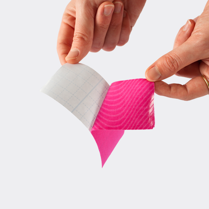 Two hands peeling a piece of pink and white patterned tape.