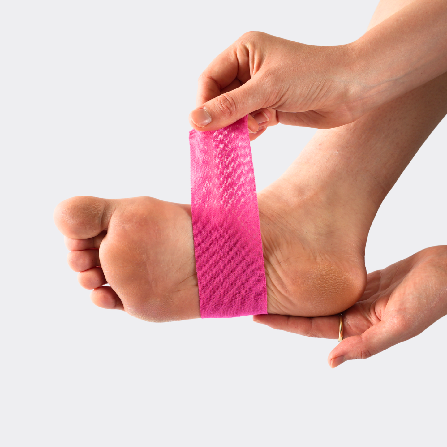 Person applying pink tape to a foot on a white background