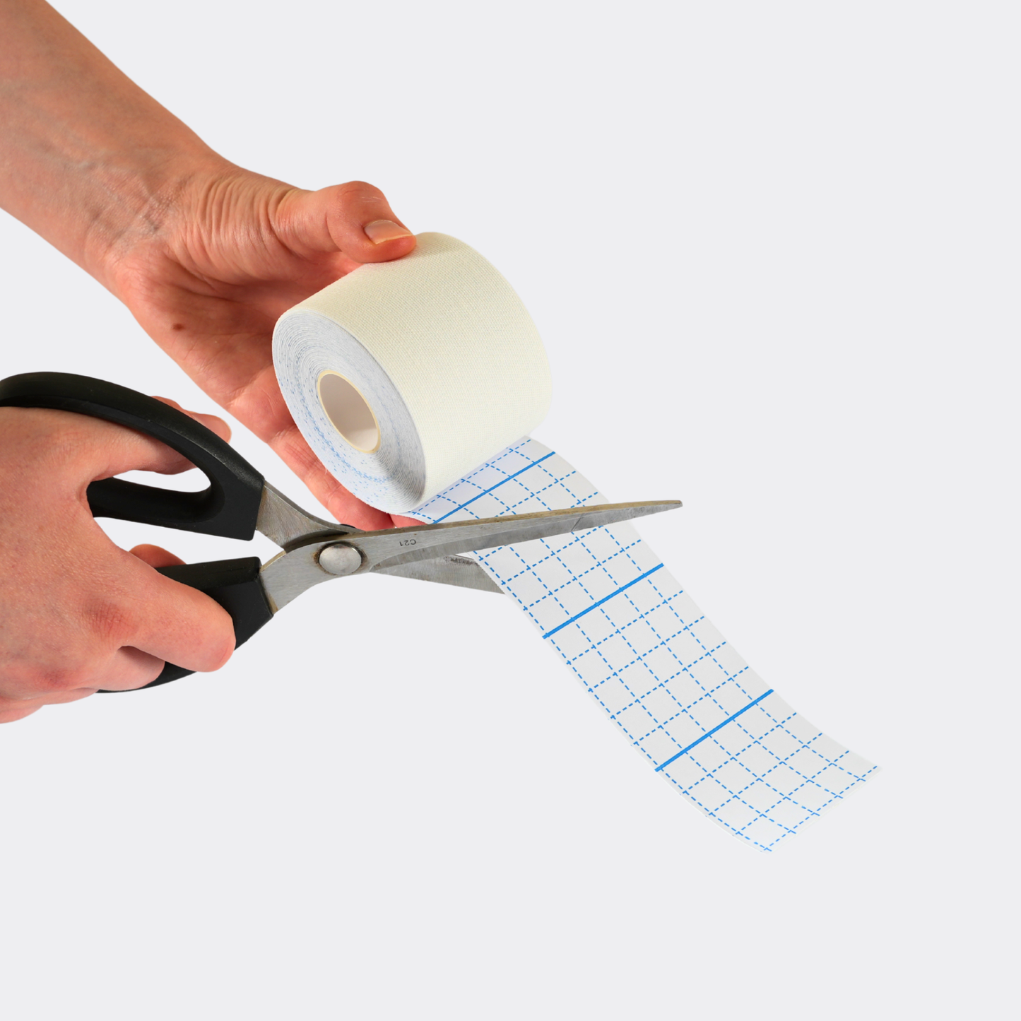 Person cutting a roll of tape with scissors on a white background