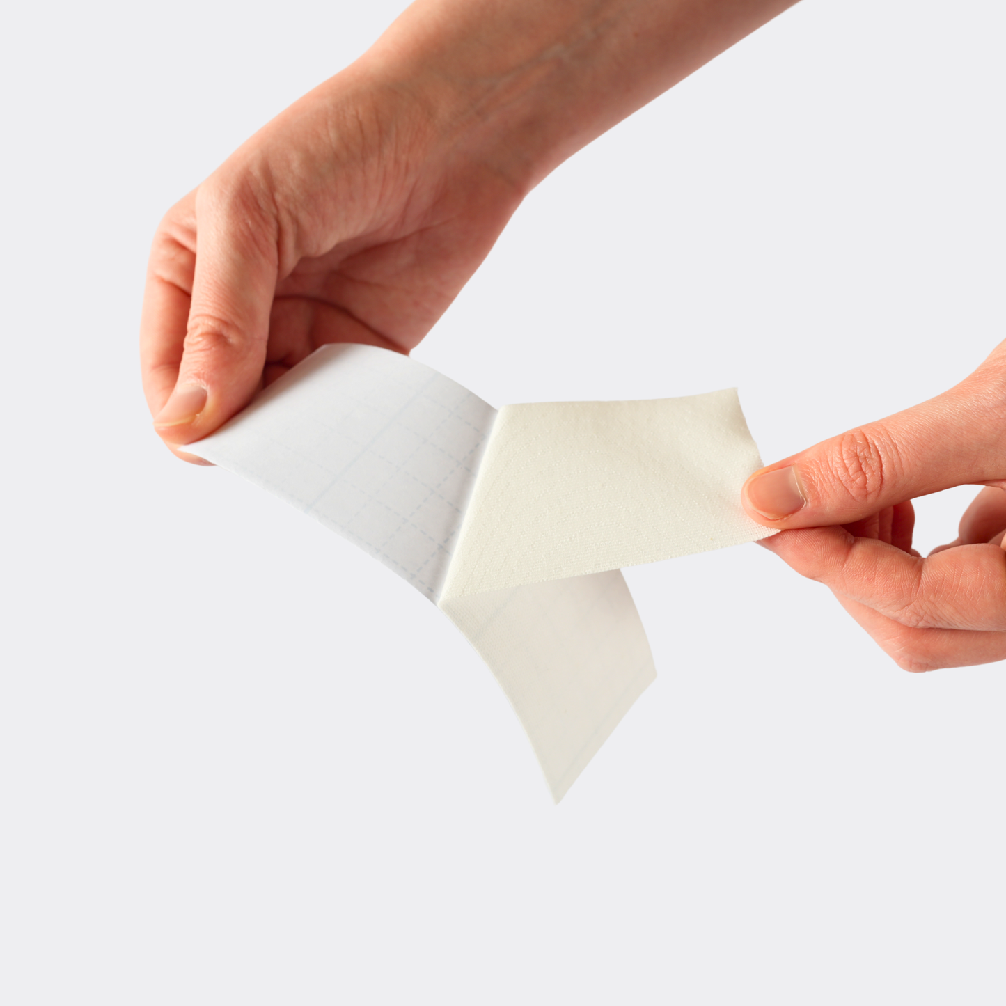 Person peeling a small white paper sheet from a larger piece on a light gray background